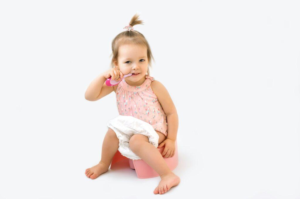Cute girl is brushing teeth with a toothbrush while sitting on a potty.