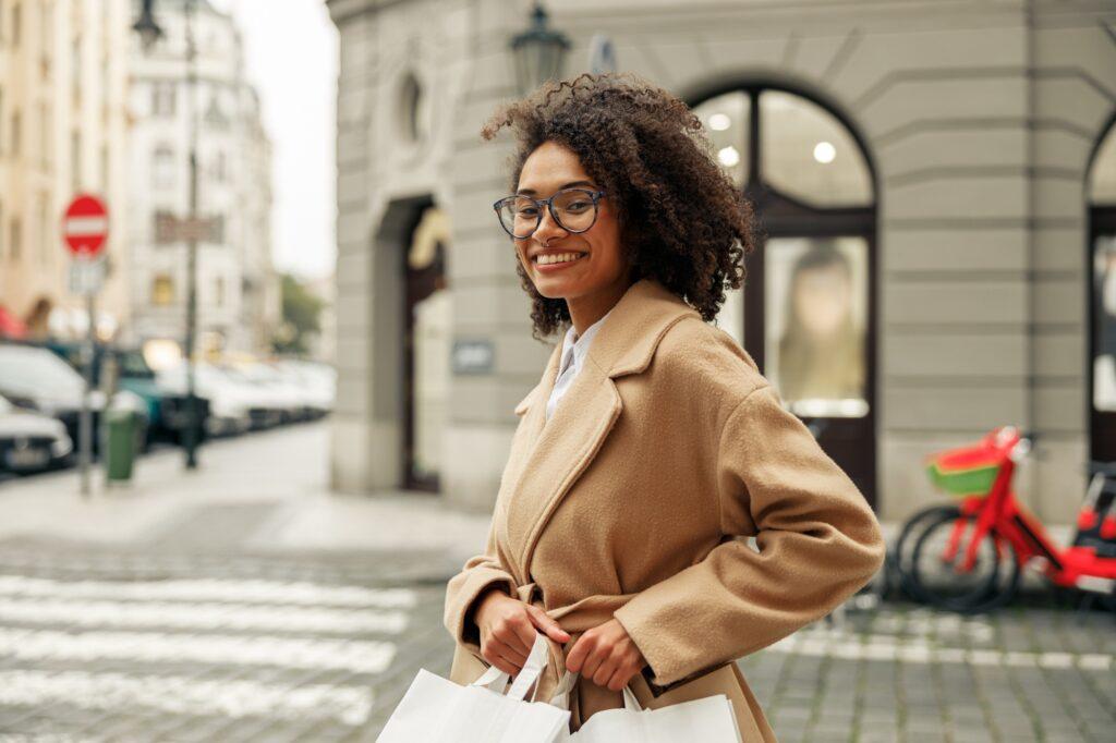 Fashion afro american woman after shopping with paper bags crosses road and looking at camera
