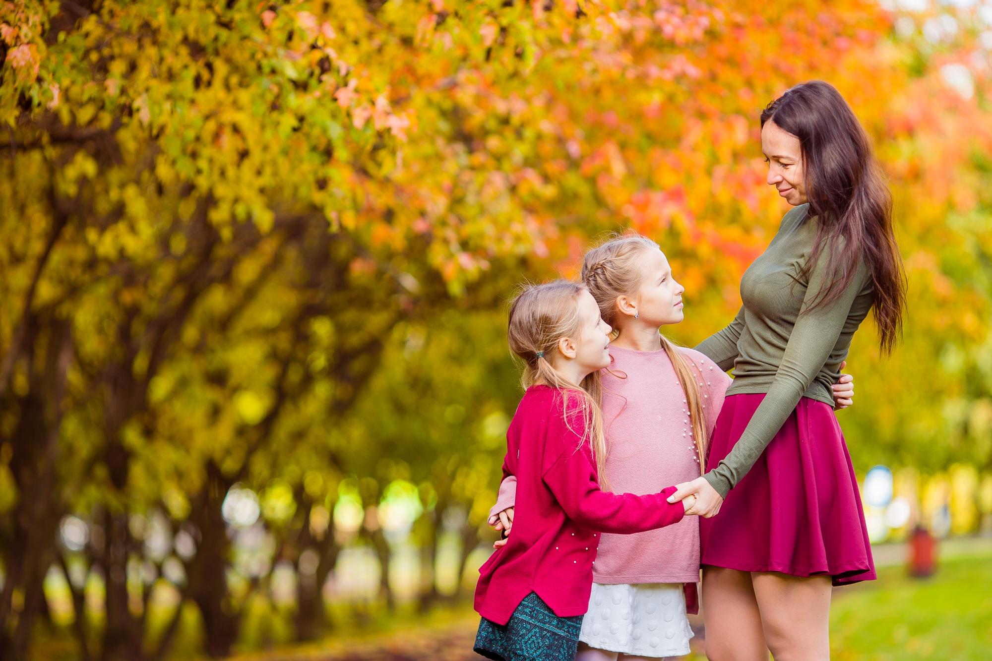 Little girl with mom outdoors in park at autumn day