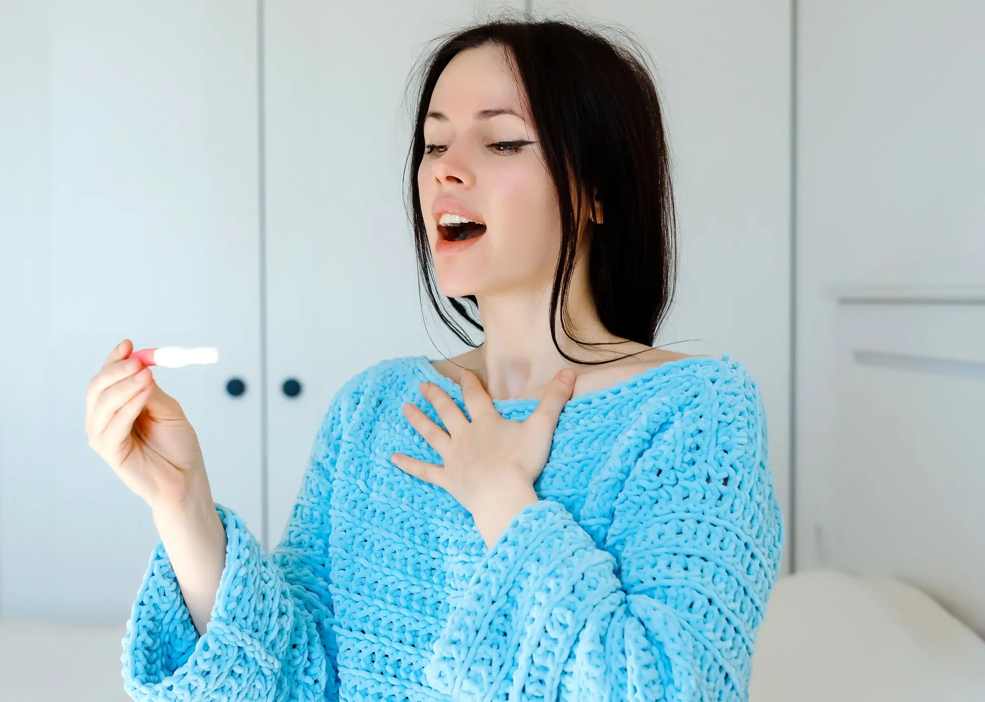 retty brunette surprised woman joyfully looking on result on pink and white pregnant test stick