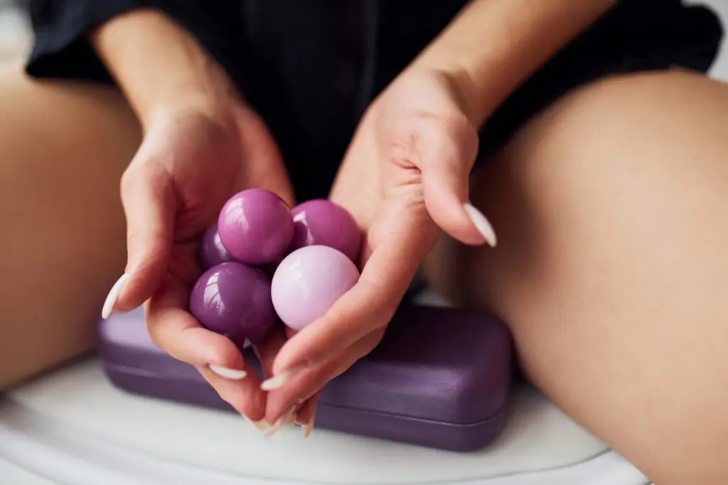 woman sits in black sexy clothes, with vaginal balls and imbuilding tools in the room