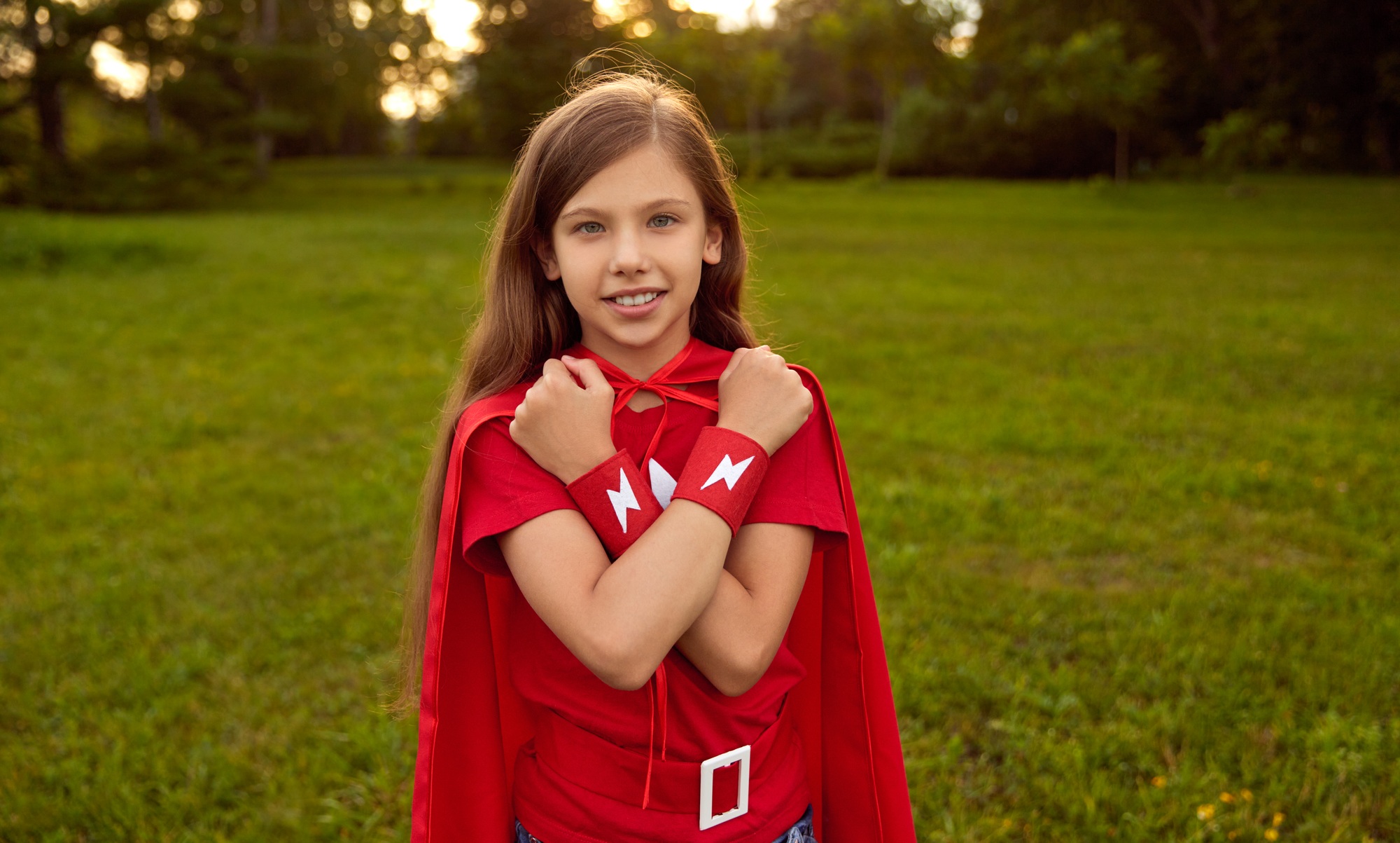 Happy girl in red superhero costume in park