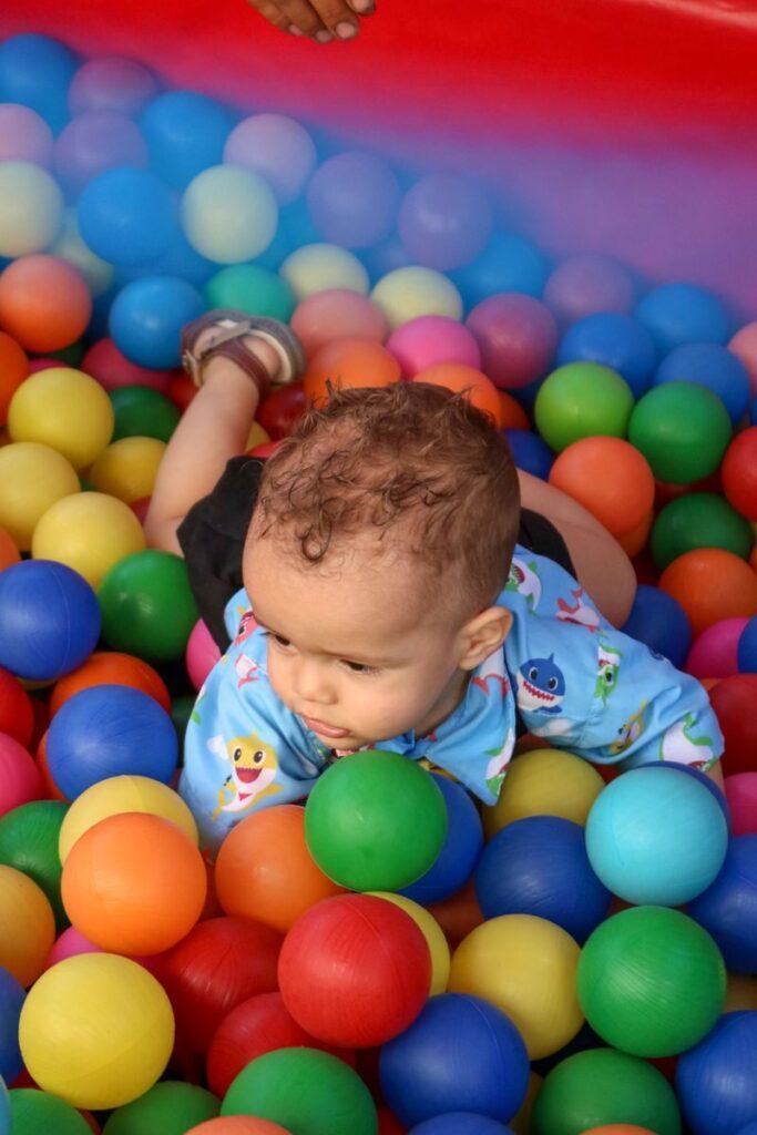 Adorable toddler crawling in a vibrant ball pit at an indoor play area.
