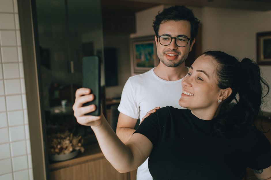 Satisfaction conjugale : 4 études sur le téléphone, les horaires et la santé A cheerful couple captures the moment with a selfie indoors, highlighting their joyful connection.