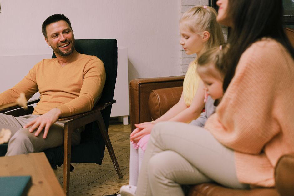 Relations positives en famille : 6 gestes pour sortir du règlement de comptes A cheerful family sitting together in the living room, sharing smiles and conversations.