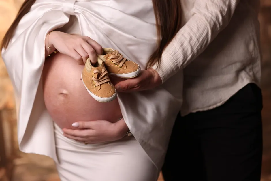 Couple après bébé : 5 repères quand le planning déborde A close-up of parents holding baby shoes on a pregnant belly, symbolizing anticipation and love.