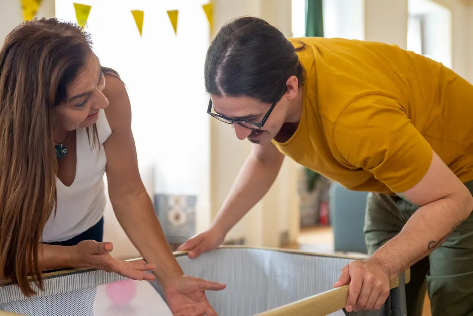 Après les enfants, traiter sa femme comme une reine : 8 gestes qui comptent A couple happily assembles a baby crib at home, smiling and engaged in conversation.