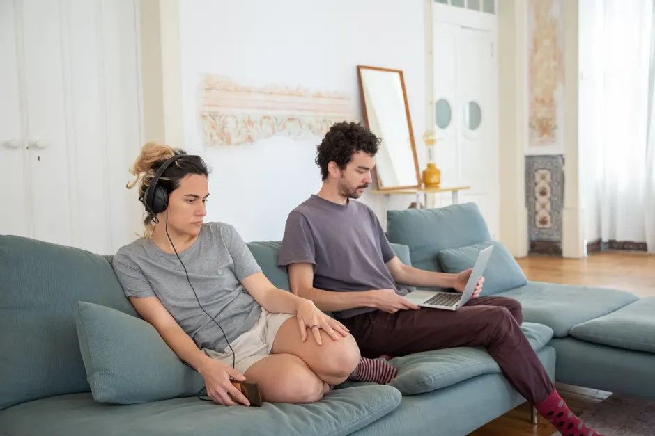 A couple relaxing on a sofa with headphones and laptop, creating a cozy home atmosphere.