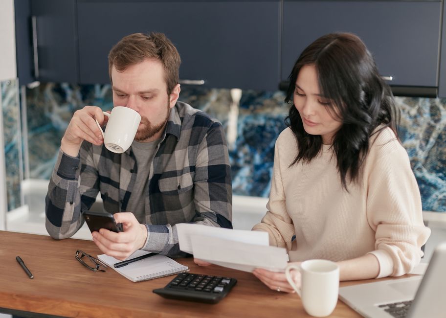 Réussir son mariage : 4 leviers quand la vie déborde A couple reviewing bills, using a calculator and smartphone, in a modern kitchen.