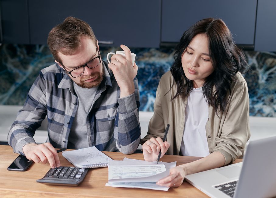 Partenaire de vie : 5 critères à observer avant de dire oui A couple reviewing household bills and budget using a calculator and laptop at their kitchen table.