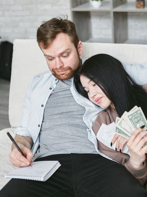 A couple sitting on a couch managing their finances, counting money and taking notes.
