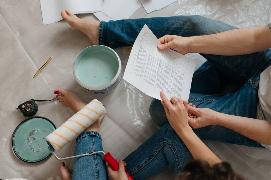 Responsabilité dans le couple : 6 repères quand la maison déborde A couple sitting on the floor planning home renovation with paint, documents, and tools.