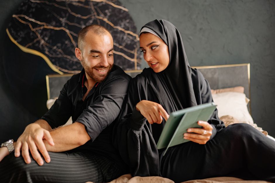 Couple durable : 5 repères concrets, sans méthode parfaite A diverse couple sitting on a bed and discussing something on a tablet indoors.