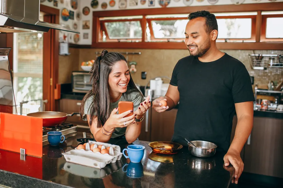 Parents de 35 à 40 ans : 100 couples face au smartphone, la satisfaction conjugale en question A joyful couple cooking breakfast together in a modern kitchen, sharing laughs and using a smartphone.