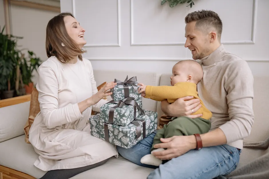Couple après bébé : 5 repères pour partager le relais A joyful family moment with parents and baby exchanging presents indoors.