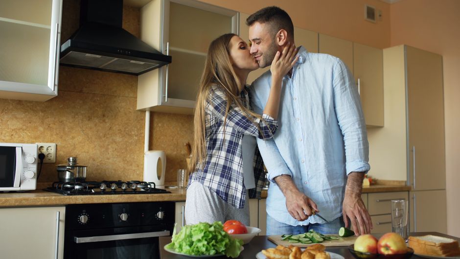 Couple et santé : 4 chiffres et un piège à éviter A loving couple kisses while preparing a meal together in their modern kitchen.
