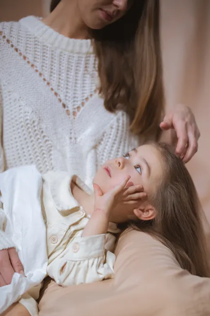 A loving mother gently strokes her child's hair while they share a serene moment indoors.