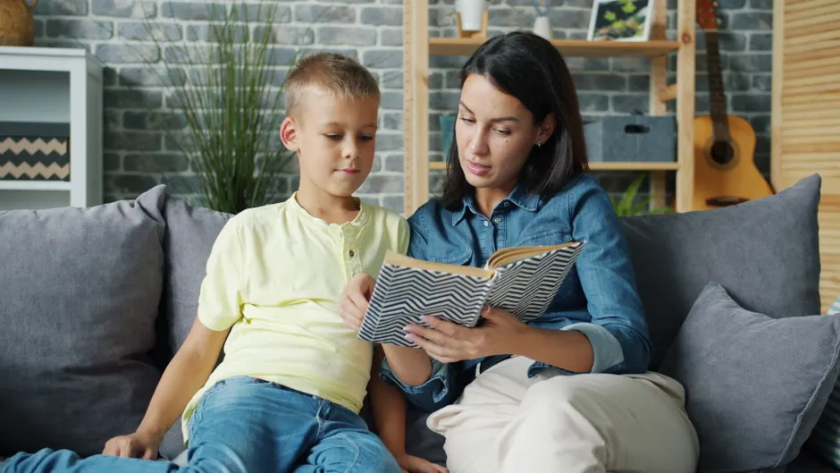 A mother and son enjoying a reading session on a cozy indoor sofa setting.