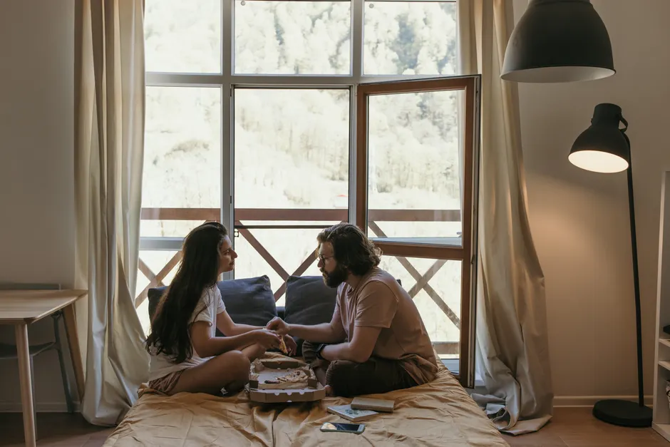 Mariage et santé : après 40 ans, ce que montrent 4 études A romantic indoor scene with a couple sharing a pizza by an open window.