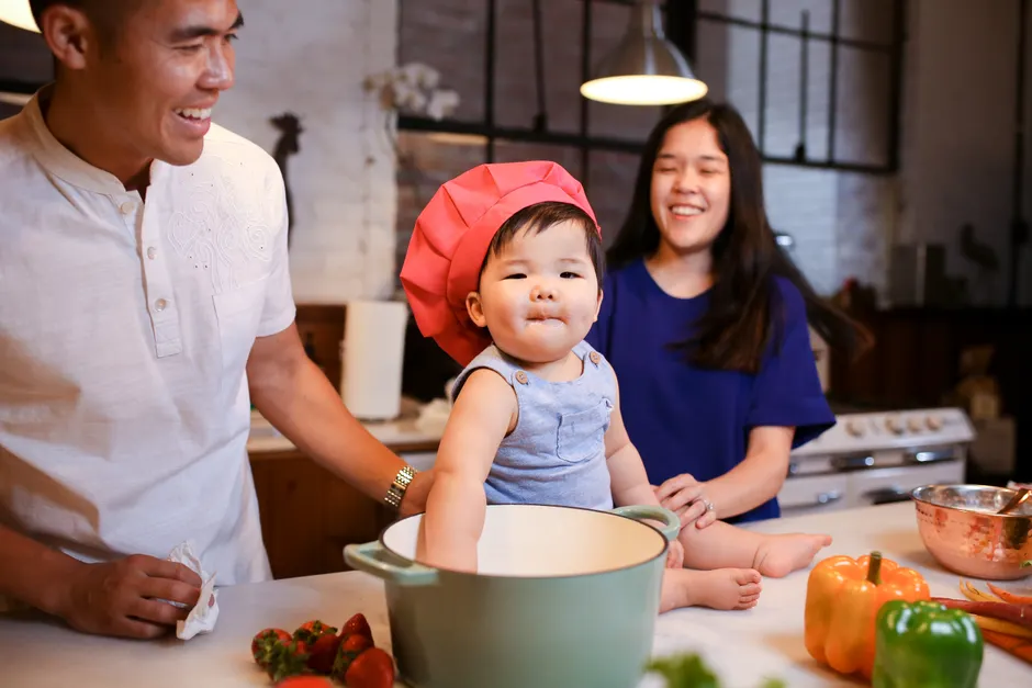 Couple après bébé : la satisfaction peut tanguer jusqu’à 5 ans, et la vaisselle n’a pas tout le dossier Adorable baby wearing chef hat with parents in a cozy kitchen setting.