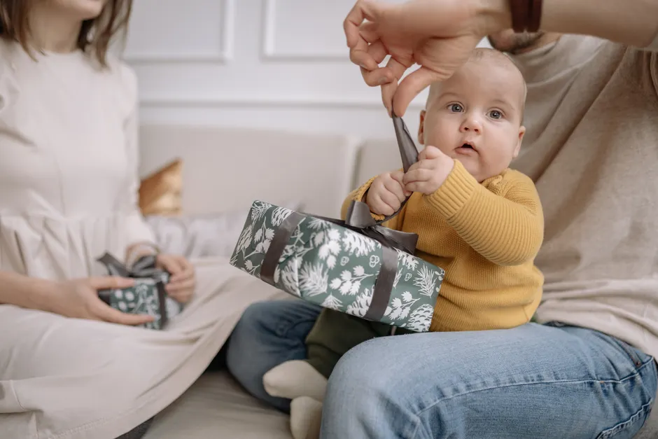 Après bébé, entretenir son couple en 5 repères, sans soirée parfaite An adorable baby with parents opening a green gift box indoors, brings a sense of warmth and family joy.