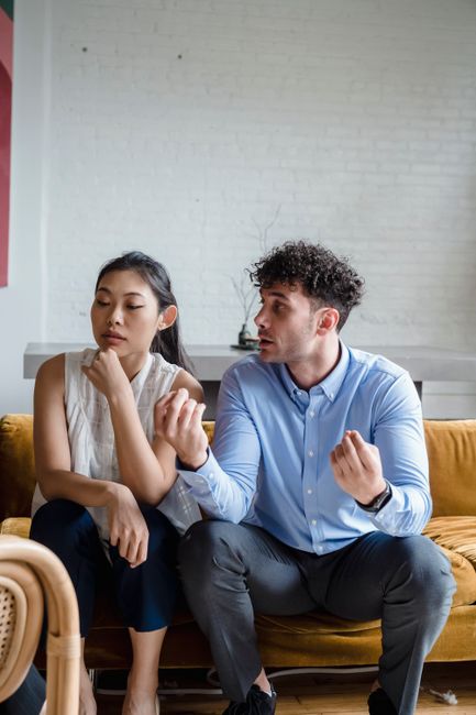 An Asian woman and Caucasian man in a serious discussion on a sofa in a modern living room.