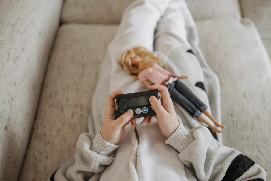 Lune de miel du diabète de type 1 chez l’enfant : l’insuline baisse, pas la vigilance Close-up of a child holding an insulin pump with a doll resting on their lap, symbolizing diabetes management in daily life.