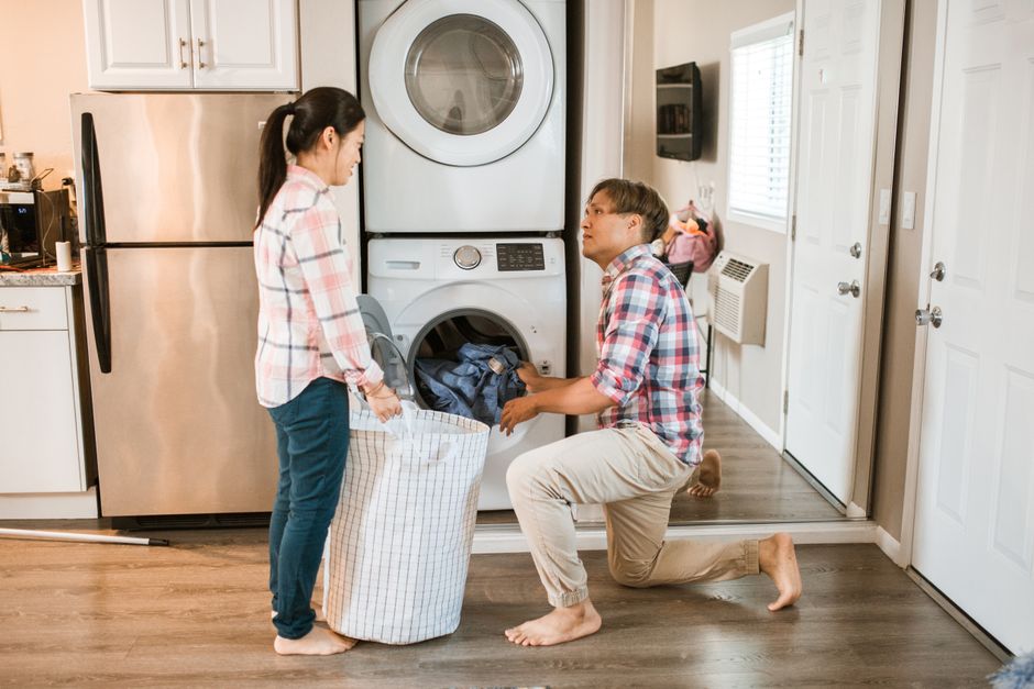 Après le mariage, 8 leçons du quotidien que les photos de noces oublient Couple managing household chores by doing laundry in a home setting.