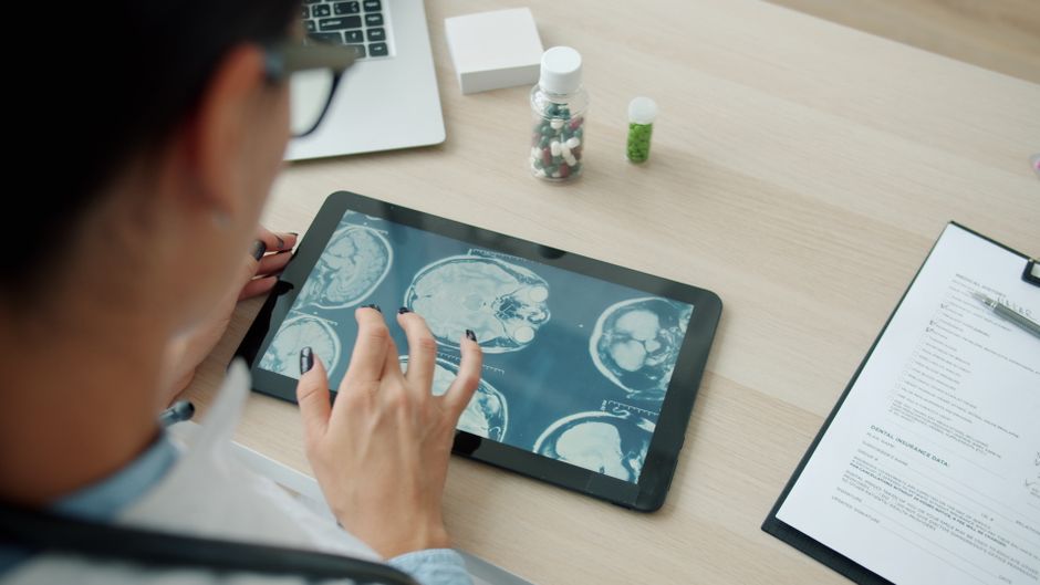 Doctor analyzing brain scans on a tablet in a clinical setting.
