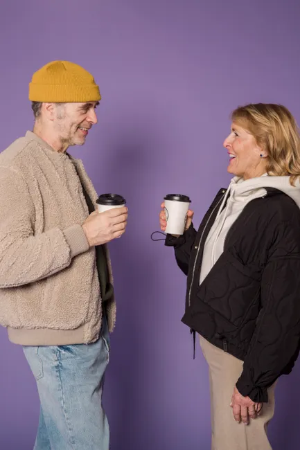 Elderly couple enjoying a casual conversation with coffee against a purple background.