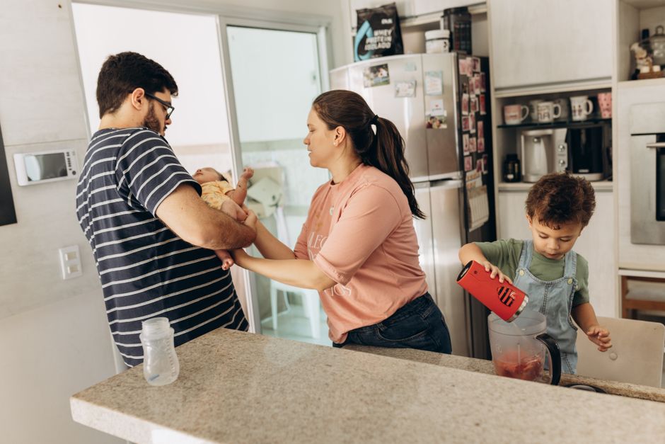 Après bébé, 5 gestes pour sortir le couple du mode coloc Family in a kitchen with parents and children engaged in daily activities together.