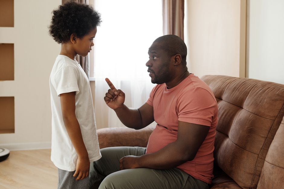 Relation de confiance : 5 repères pour créer du lien sans forcer Father and son engaged in a heartfelt conversation on the sofa, illustrating parenting in a loving family setting.