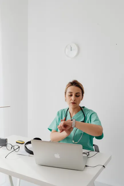 Female doctor in scrubs checks her watch while working in an office environment.