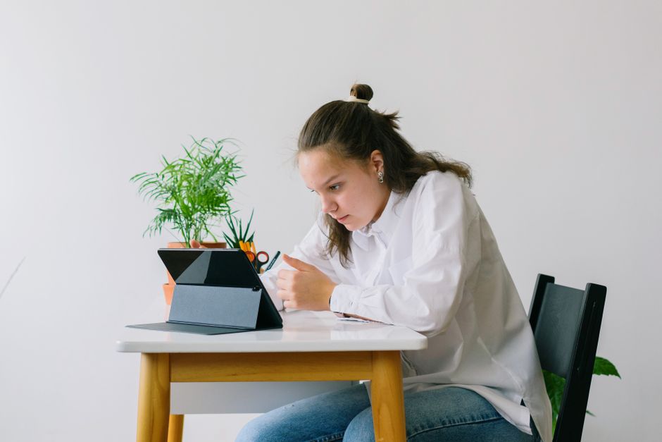 À 14-16 ans, la persévérance scolaire vacille : le grit ne fait pas tout Focused teenager girl studying with a tablet at home. Bright, minimalistic indoor setting with plants.