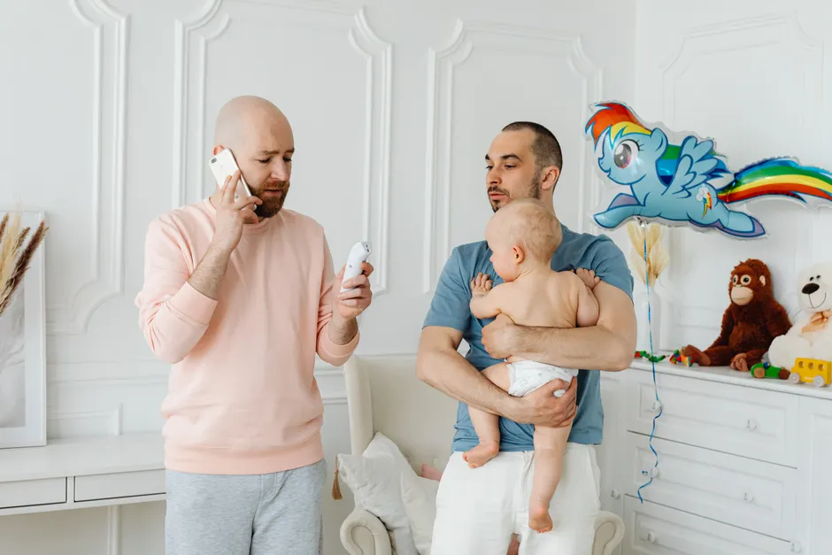 Couple après bébé : 5 pistes pour se retrouver sans grand numéro de cirque Gay couple nurturing their baby at home, with toys and decor creating a cozy family environment.