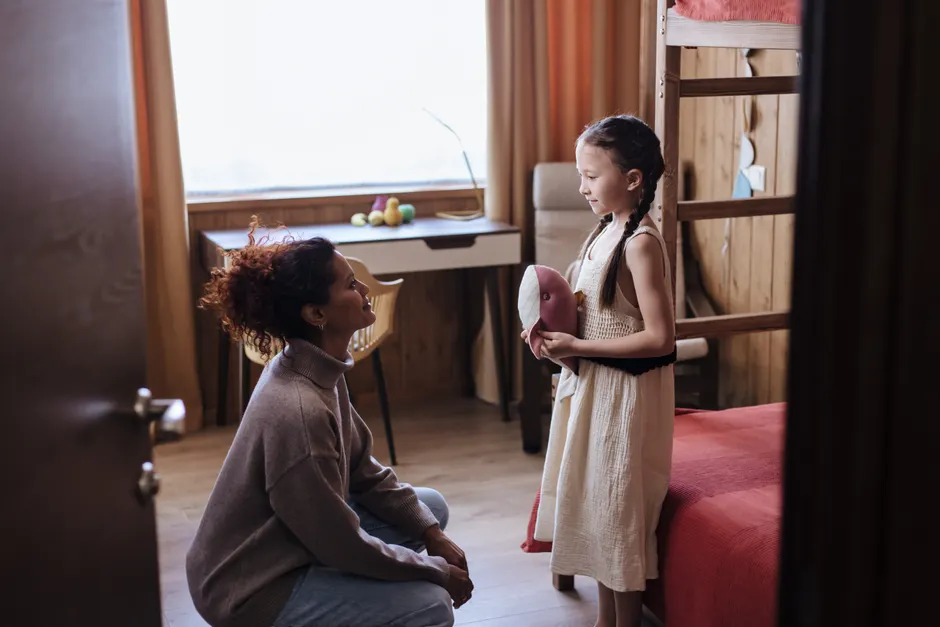 Conseils de maman: 687 adultes autour de 49 ans, entre aide et pression Mother kneeling and talking to her daughter in a cozy home interior, fostering a loving family bond.