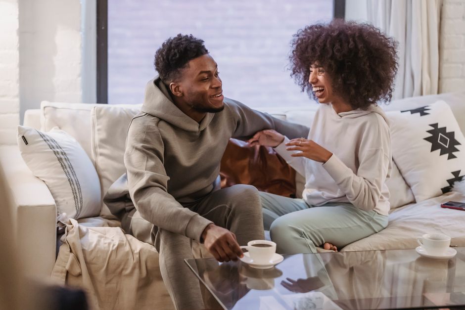 Désir sexuel dans le couple : 4 repères quand l’envie ne suit pas le planning familial Positive African American couple talking and laughing on comfortable sofa at home in daytime