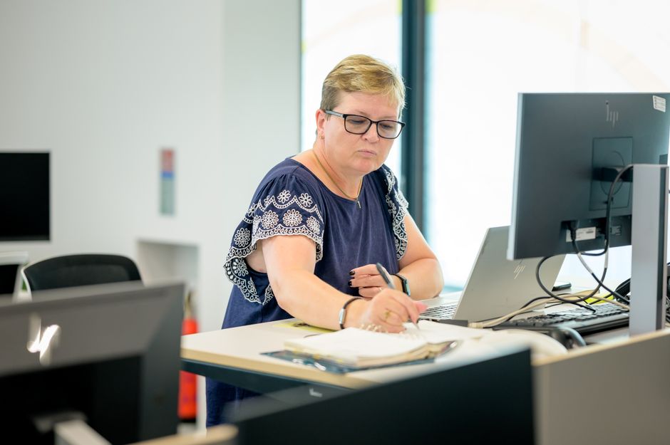 Femmes autistes au travail : 3 attentes et un cadre à revoir Professional woman wearing eyeglasses working at an office desk with a laptop and notebook.
