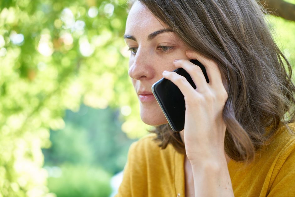 Après 45 ans, l’AVC passe au SMS: Love Your Brain à l’essai Side profile of a woman using a smartphone outdoors in a sunlit park, wearing a yellow top.