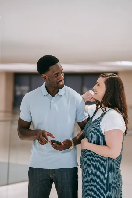 Smiling interracial couple interacting with a mobile phone inside a modern building.