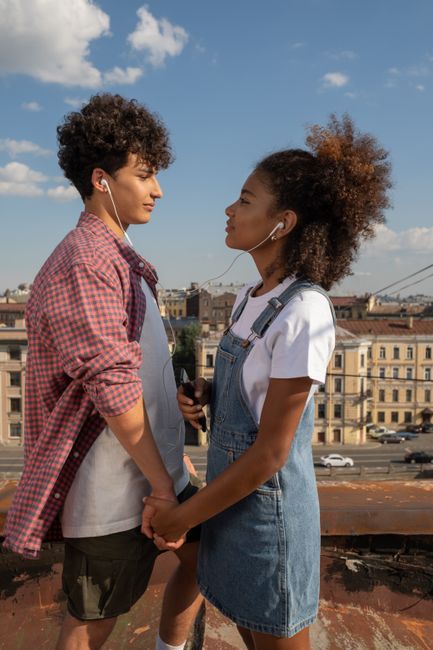 Young couple holding hands on a city rooftop, listening to music together, feeling love and connection.