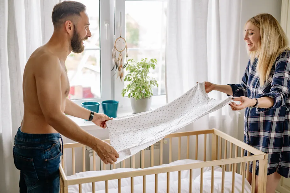 Green flags en couple : 8 signes qui rassurent, même quand la vie déborde A cheerful couple setting up a crib in a sunlit bedroom, symbolizing family and domestic life.