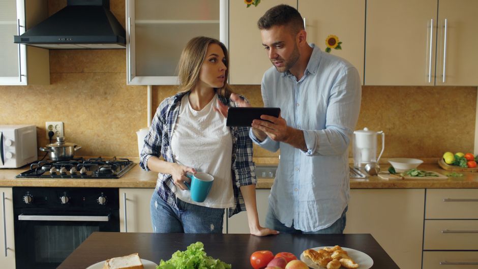 Les 5 étapes d’une relation : du flirt à l’engagement, sans GPS A couple discusses meal plans in a modern kitchen using a tablet.