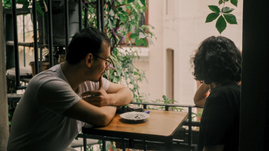 A couple enjoys a relaxed conversation on a leafy urban balcony setting.
