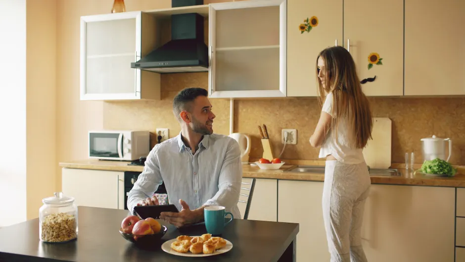 Habitudes de couple : 8 gestes quand tout déborde A couple having breakfast in a modern kitchen with sunlight streaming in.