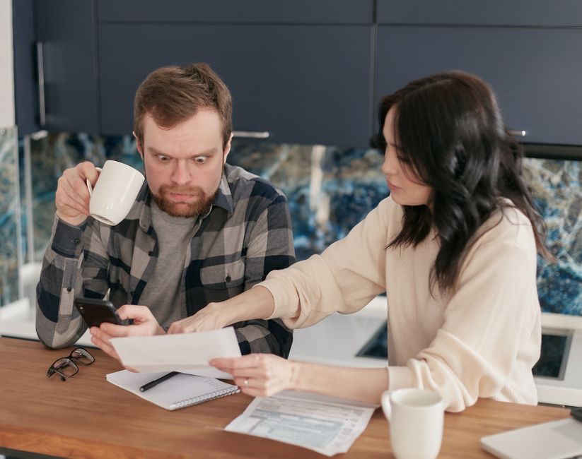 Emménager, se marier, devenir parents : 3 virages de couple avant que la vaisselle ne tranche A couple reviews household bills in a kitchen, appearing concerned and focused.