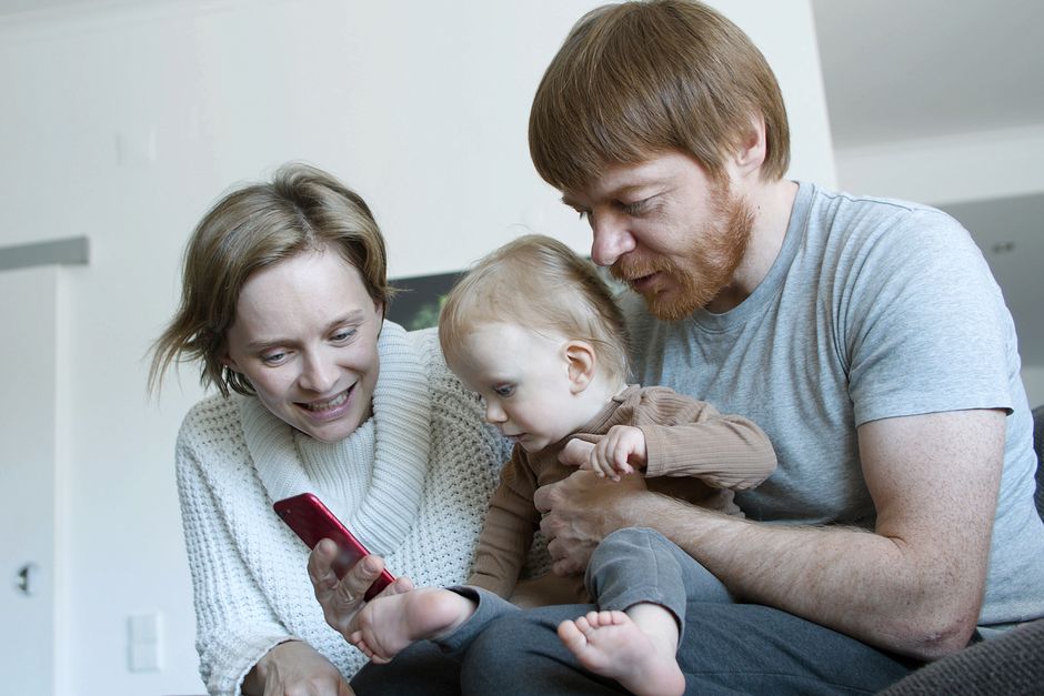 Après bébé, le couple vacille : 4 repères concrets A family enjoying quality time together at home, interacting with a smartphone.