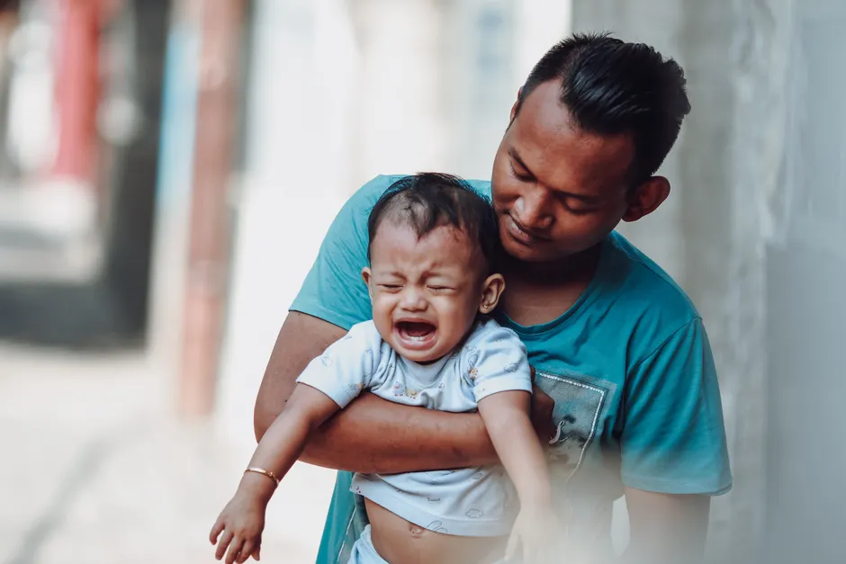 Roue des émotions : 3 étapes pour aider l’enfant à parler, sans jouer au psy A father lovingly holds his crying baby boy outdoors, creating a tender parenting moment.