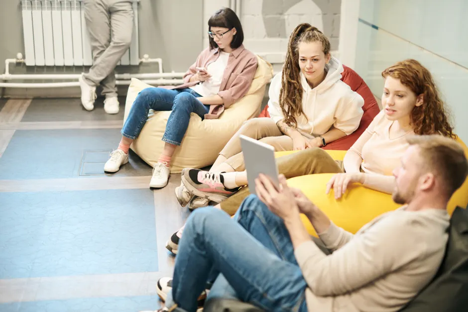 Amour romantique : 808 jeunes adultes face aux clichés A group of young adults socializing indoors, sitting on bean bags, engaging with a tablet.