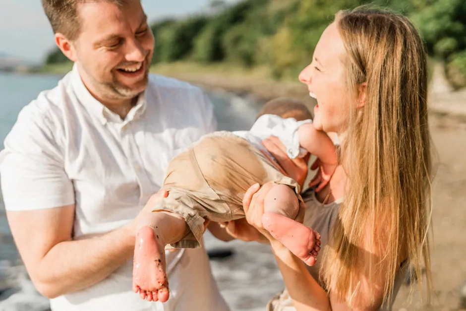 Humour dans le couple après bébé : 3 études pour distinguer la blague de la pique A happy family enjoying time together at the beach, laughing and playing.